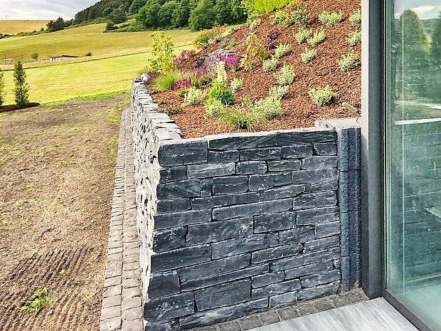 Ein Natursteinsockel strukturiert das Gelände 